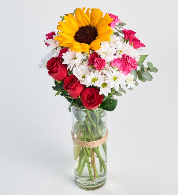 Rosas y margarita blanca y girasol en jarrón de cristal