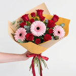 Red gerbera daisies and orange spray roses in a yellow bouquet